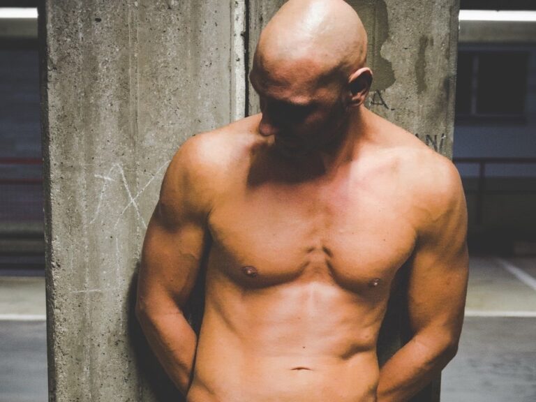 Shirtless man leaning on concrete pillar
