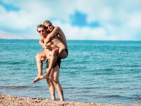 May December gay couple piggyback on beach