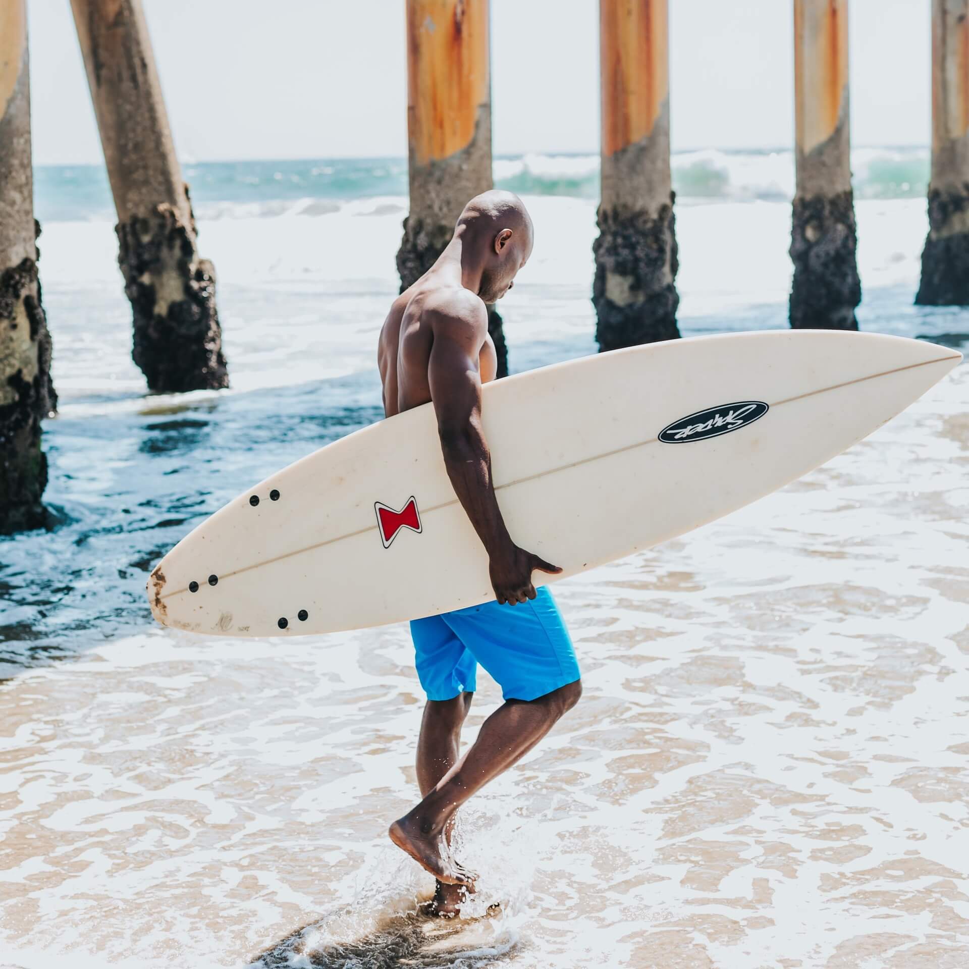 Shirtless surfer walking under pier
