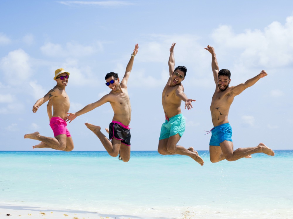 Four men in swim trunks jumping high in unison on beach Four men in swim trunks jumping high in unison on beach